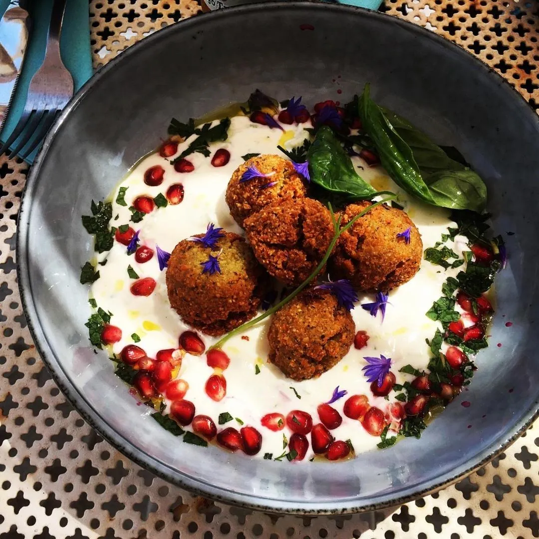 Assiette de falafels décorés de yaourt, de grenade et de fleurs.