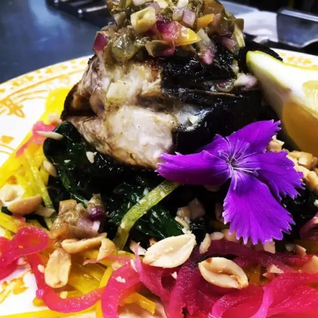 Assiette de poisson grillé garnie de légumes et de fleurs.
