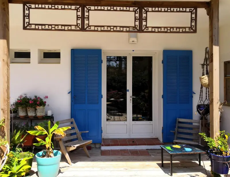Façade blanche avec des volets bleus et une terrasse fleurie.