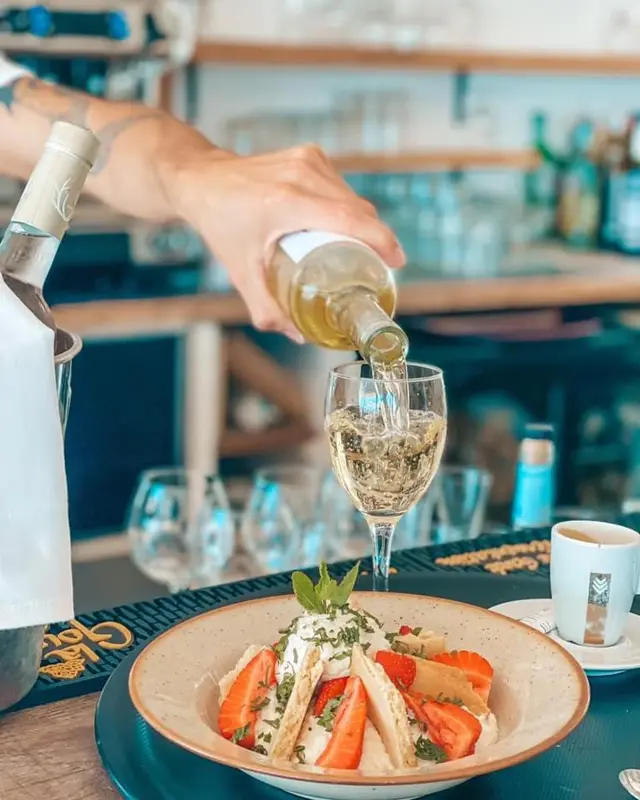 Un serveur verse du vin dans un verre à côté d'une assiette de dessert.