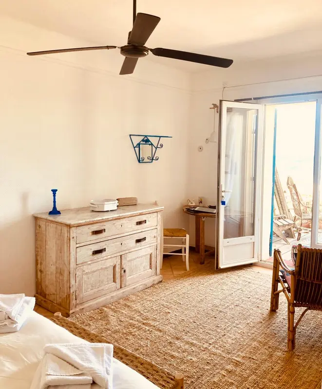 Une chambre lumineuse avec un bureau en bois et une porte ouverte sur une terrasse.