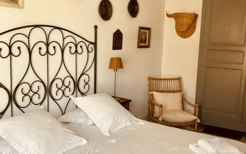 Une chambre lumineuse avec un lit à baldaquin en fer forgé et une chaise en rotin.