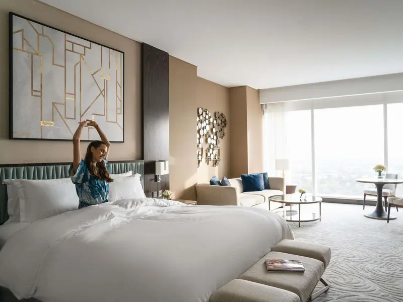 Une personne s'étire dans une chambre lumineuse avec un grand lit et un coin salon.