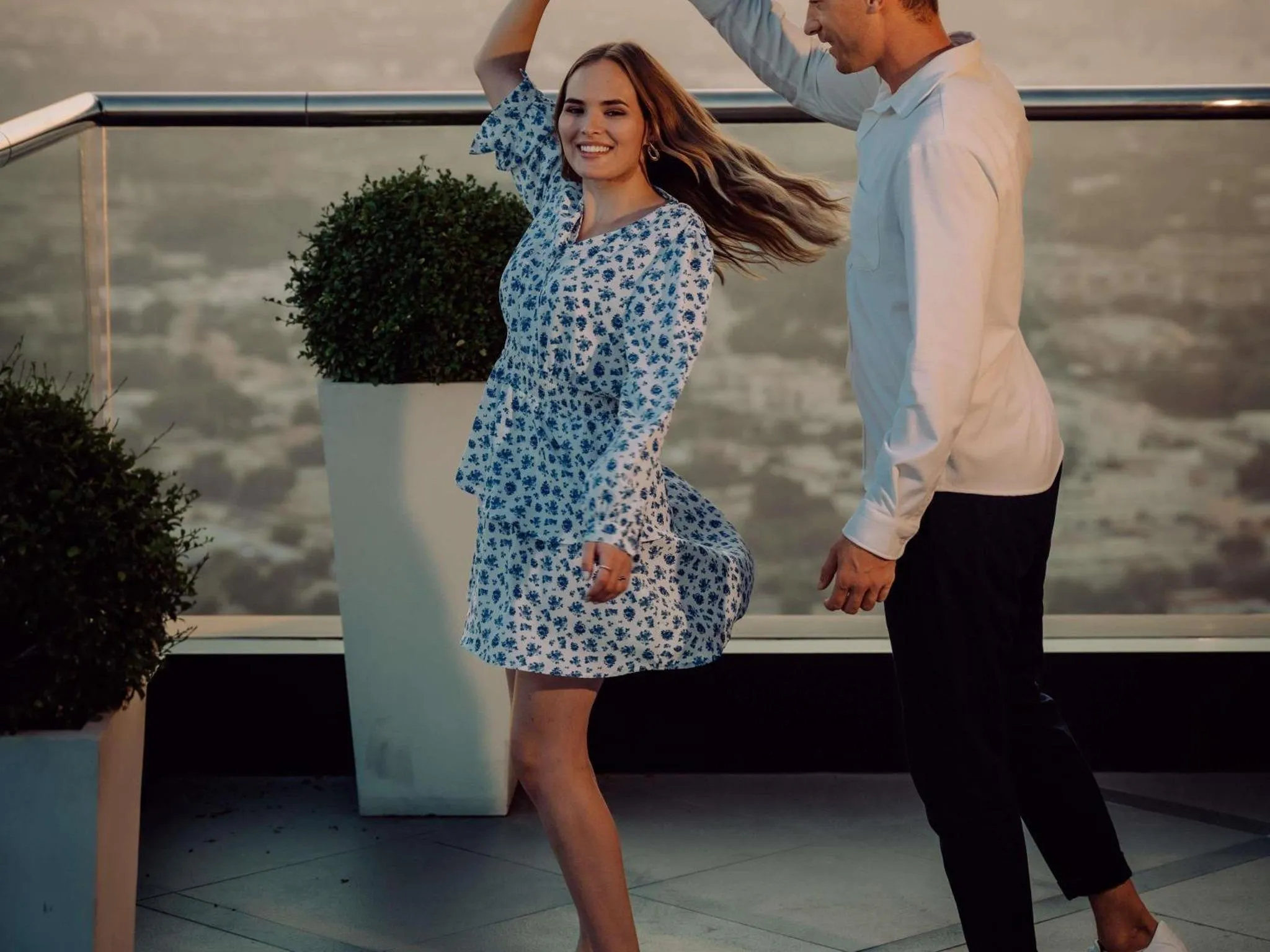 Un couple danse sur une terrasse ensoleillée avec vue sur la mer.