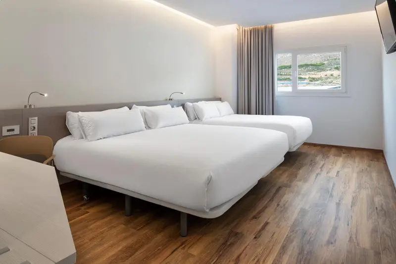 Chambre lumineuse avec deux lits simples et une vue sur un paysage.