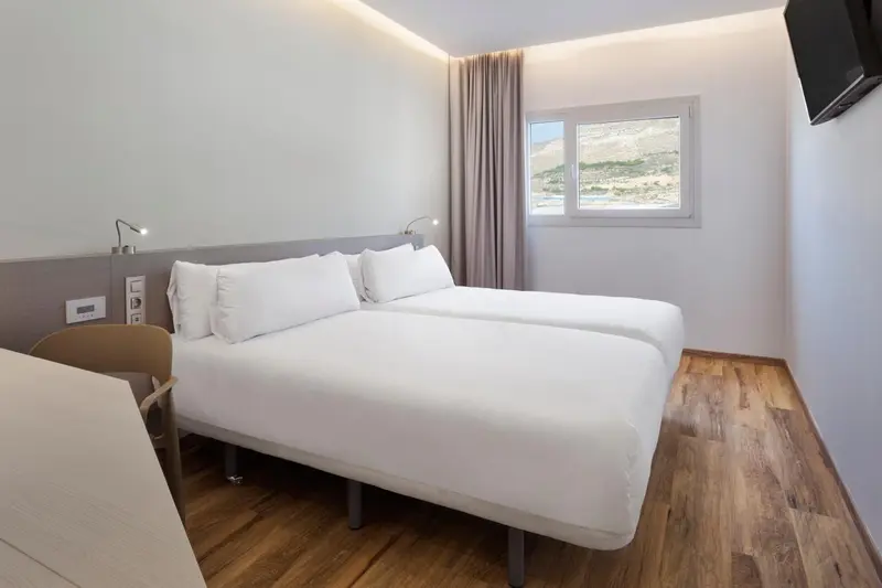 Une chambre lumineuse avec un grand lit et une fenêtre offrant une vue sur le paysage.