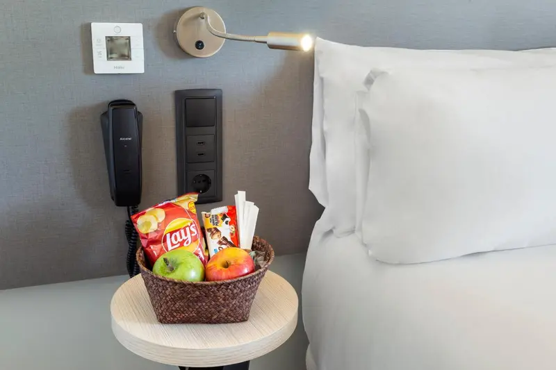 Un lit blanc avec une table de chevet et un téléphone fixé au mur.