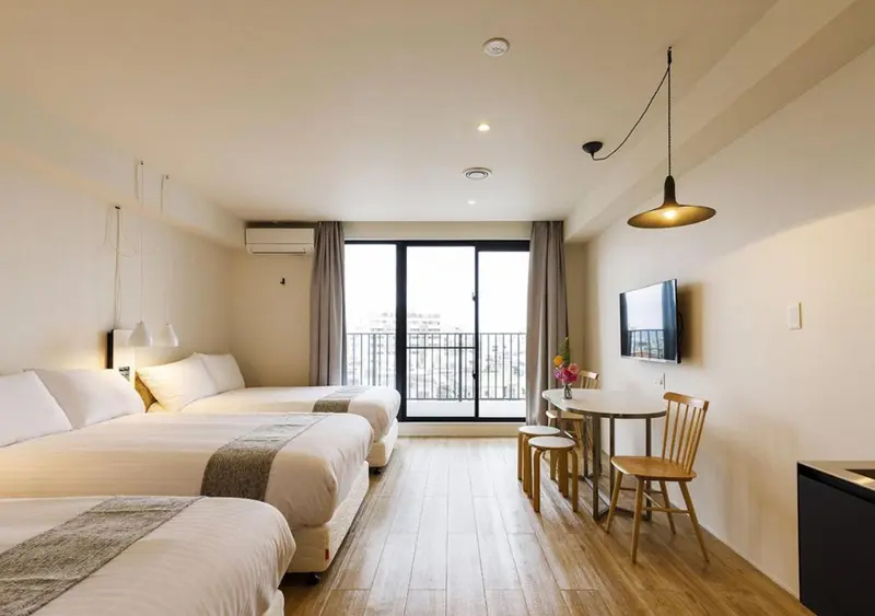 Une chambre lumineuse avec deux lits et un coin repas près d'une fenêtre.