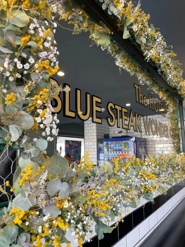 Façade d'un établissement ornée de guirlandes florales et d'une enseigne lumineuse.