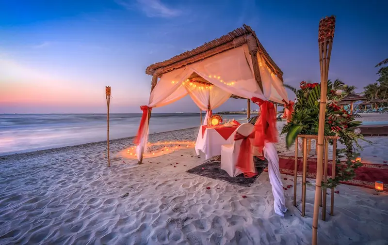 Table romantique dressée sur une plage au coucher du soleil.