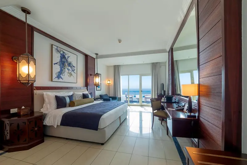 Chambre avec un grand lit et vue sur la mer par une baie vitrée.