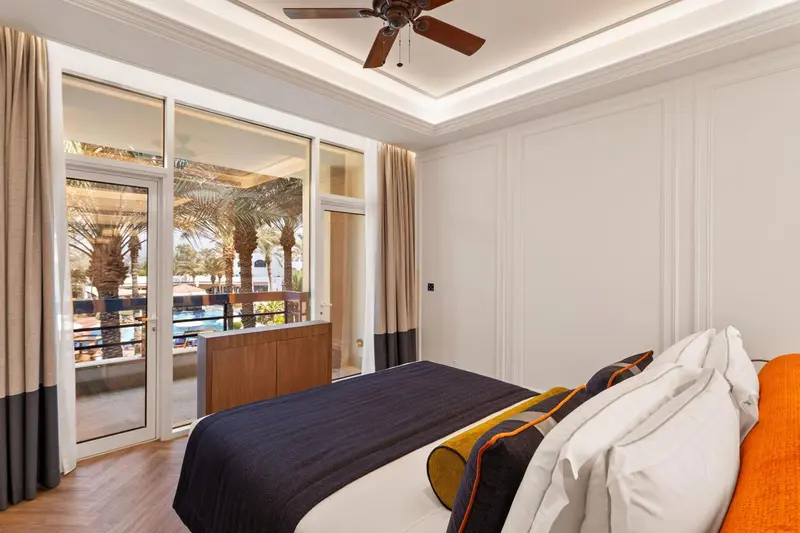 Une chambre lumineuse avec un grand lit et une vue sur une piscine et une végétation tropicale.