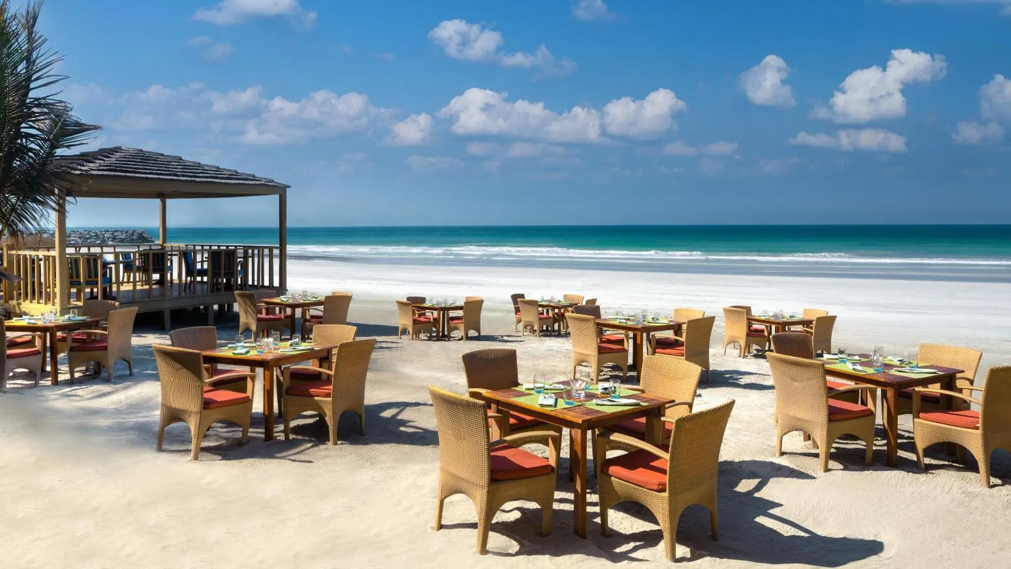 Tables et chaises disposées sur une plage de sable blanc face à la mer.