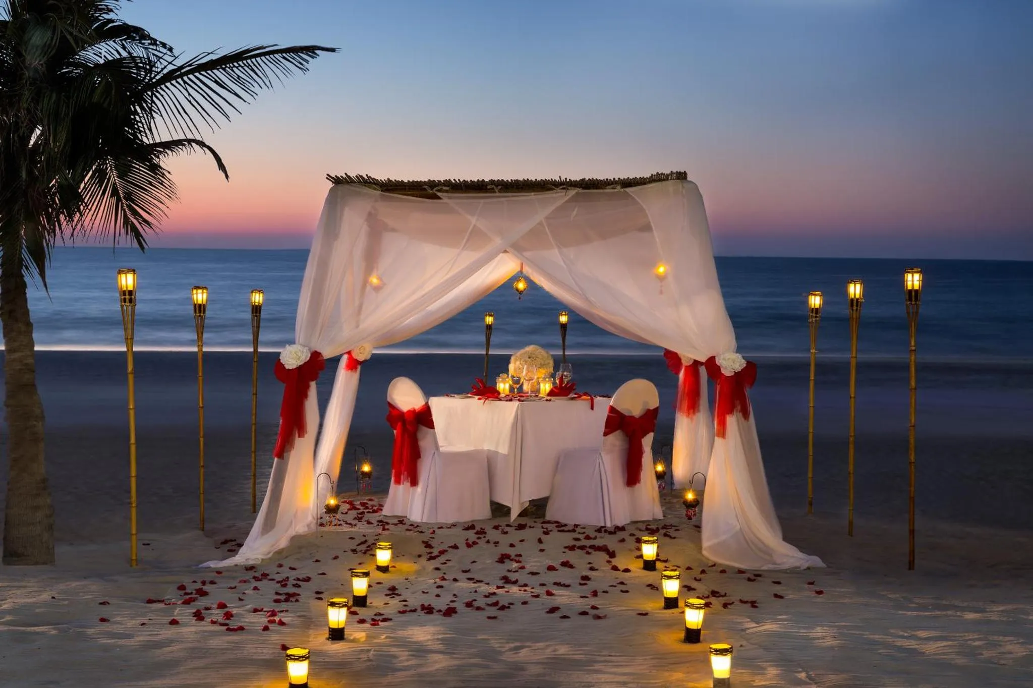 Table romantique dressée sur une plage au coucher du soleil.