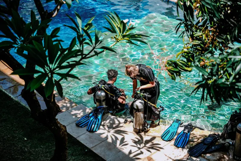 Deux personnes équipées près d'une piscine ensoleillée.