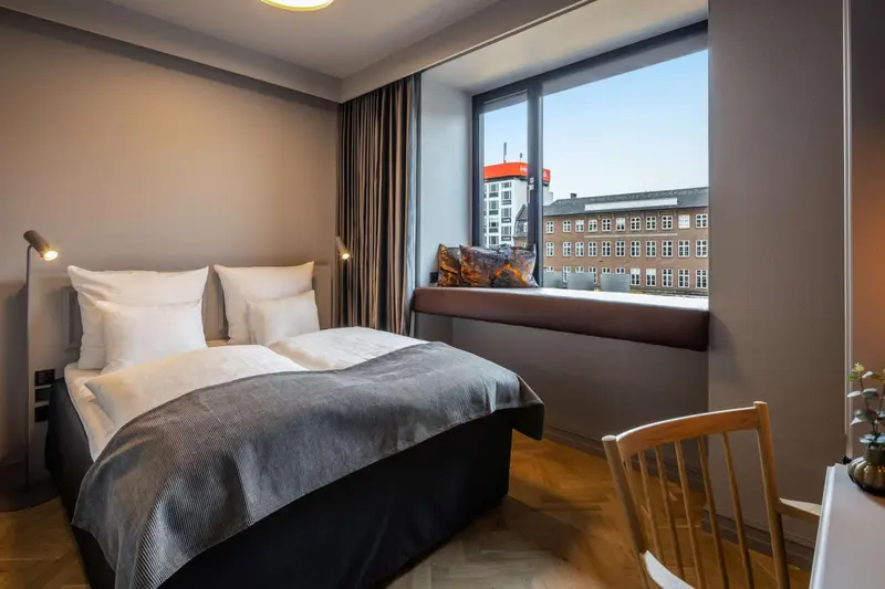 Une chambre avec un lit double et une fenêtre donnant sur une vue urbaine.