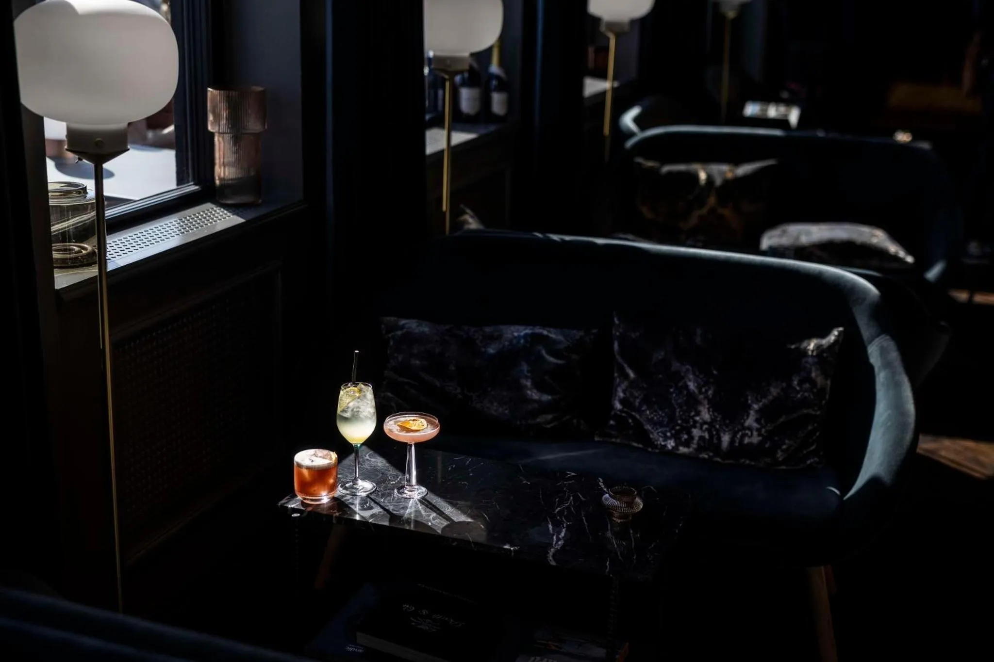 Un cocktail est posé sur une table basse devant un canapé en velours sombre.