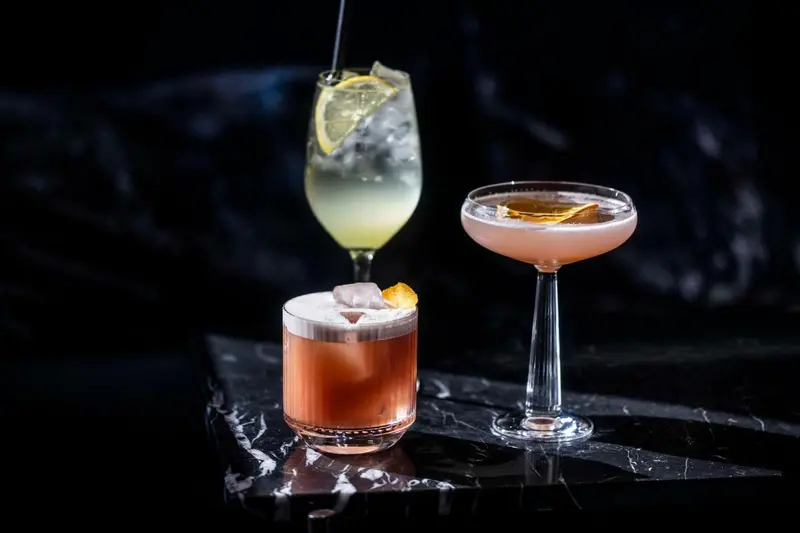 Trois cocktails colorés présentés sur une surface sombre et marbrée.
