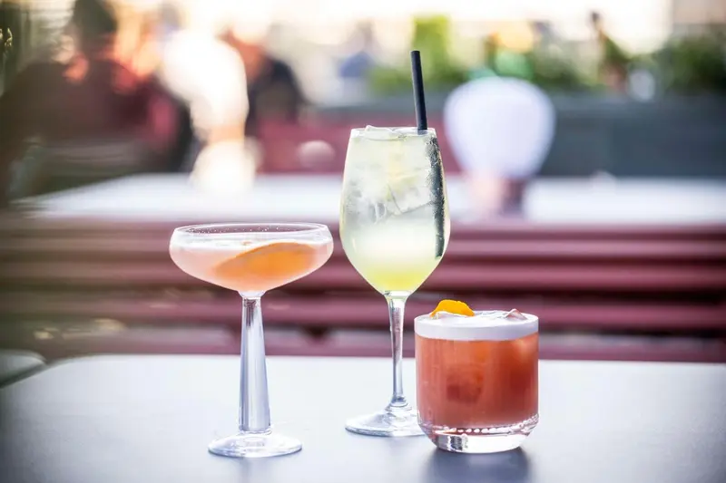 Deux cocktails et une boisson rafraîchissante sur une table en extérieur.