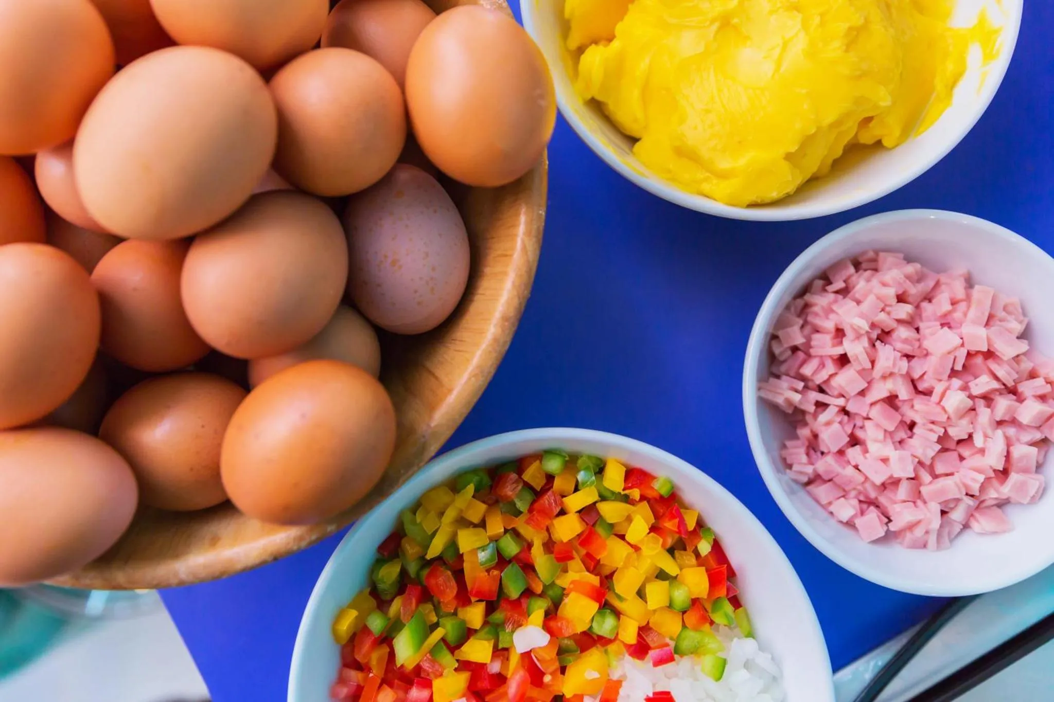 Des œufs, du jambon coupé en dés et des légumes colorés sont présentés dans des bols.