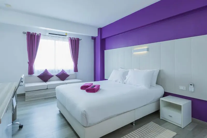 Une chambre lumineuse avec un grand lit et un canapé mauve.
