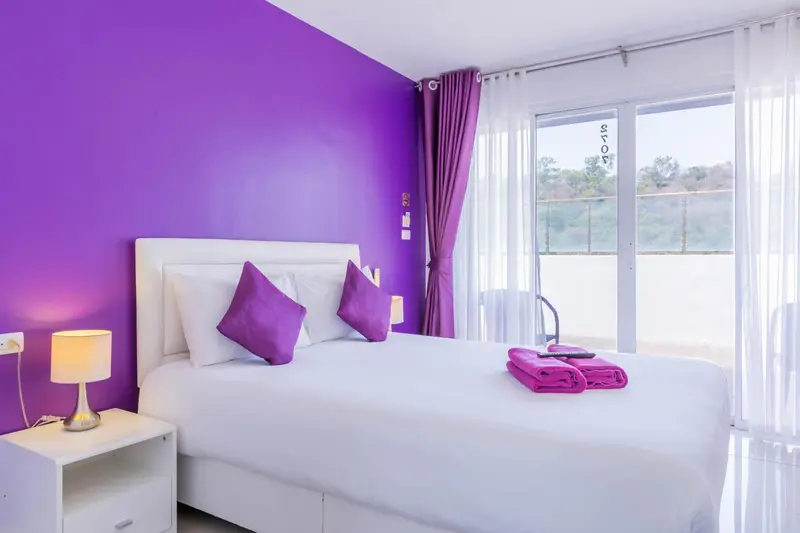 Une chambre lumineuse avec un lit blanc et des touches violettes.