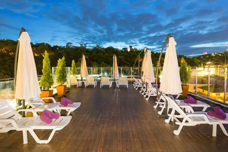 Terrasse aménagée avec transats et parasols blancs, vue sur la ville illuminée.