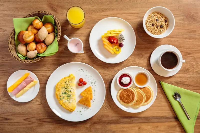 Une table en bois présente un petit-déjeuner copieux avec des viennoiseries, des fruits et des plats chauds.