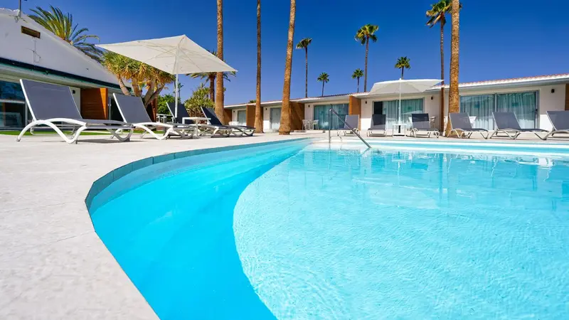 Transats et parasols bordent une piscine turquoise dans un cadre tropical.