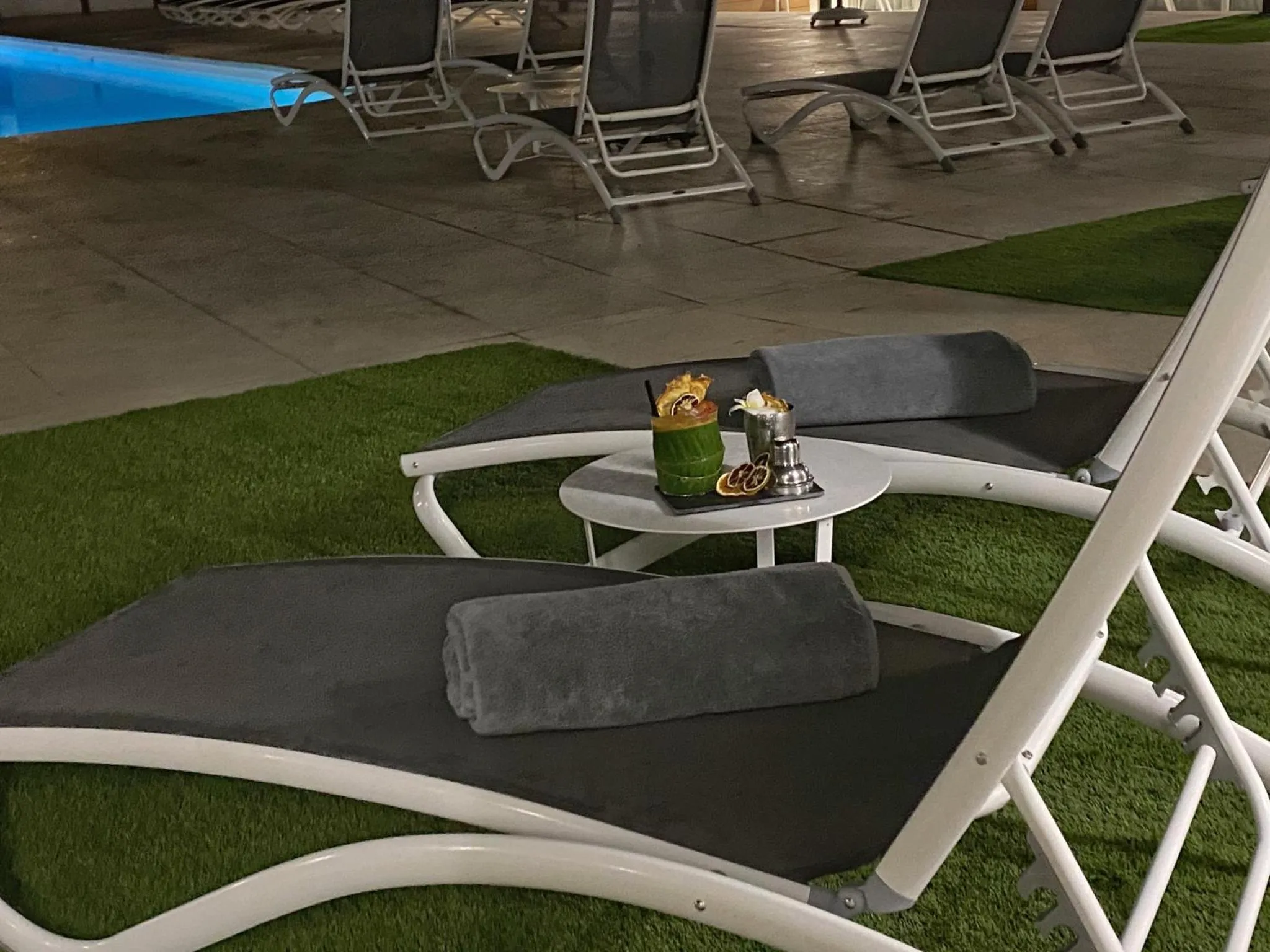 Transats et table basse avec boissons au bord d'une piscine.