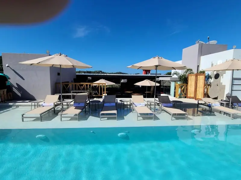 Transats et parasols bordent une piscine turquoise sous un ciel bleu dégagé.