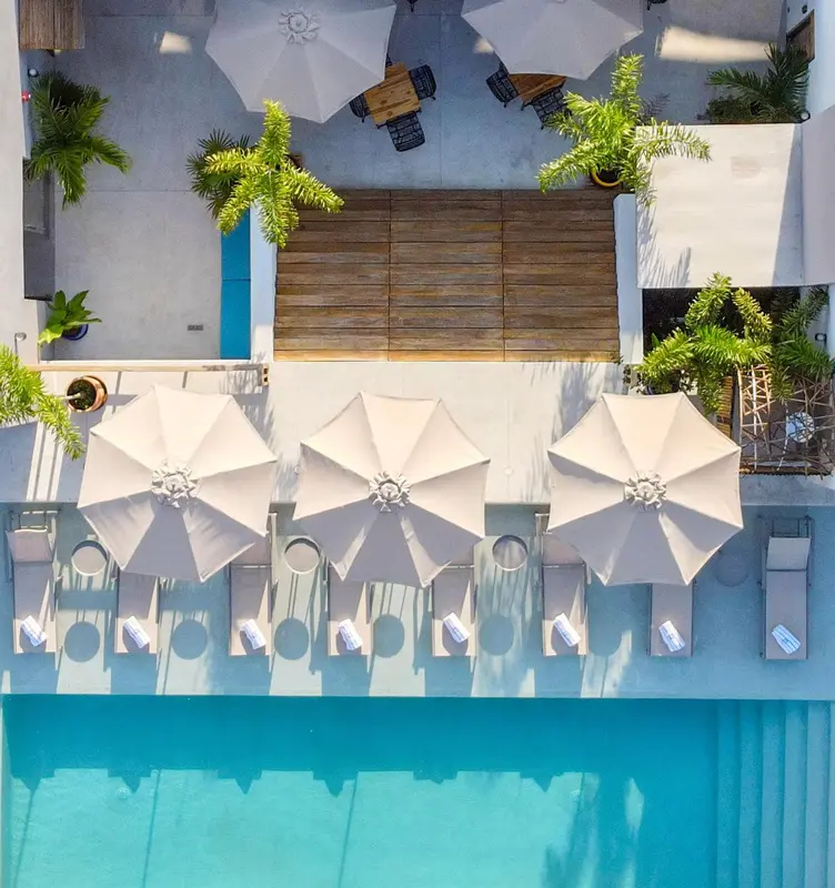 Vue aérienne d'une piscine bordée de transats et de parasols blancs.
