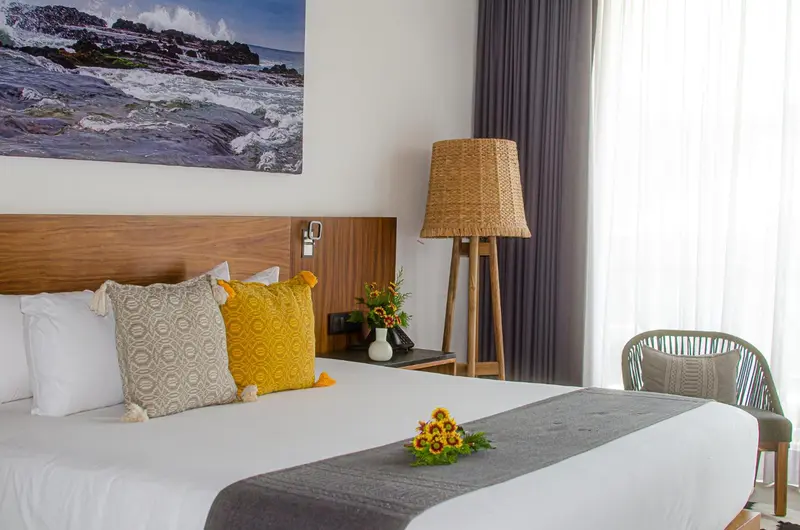 Une chambre lumineuse avec un lit décoré de coussins et une vue sur la mer.
