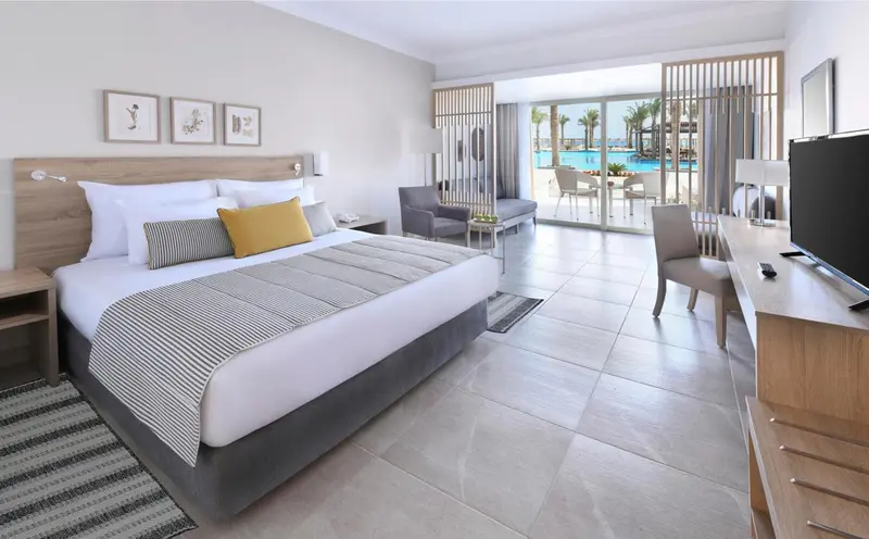 Une chambre lumineuse avec un grand lit et un accès à une terrasse avec vue sur une piscine.