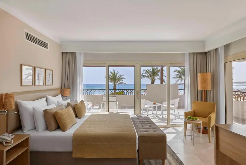 Une chambre lumineuse avec un grand lit donnant sur une terrasse et la mer.