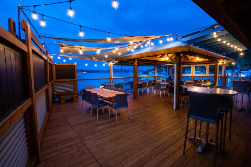 Terrasse en bois avec tables et chaises illuminée par des guirlandes lumineuses, vue sur la mer.