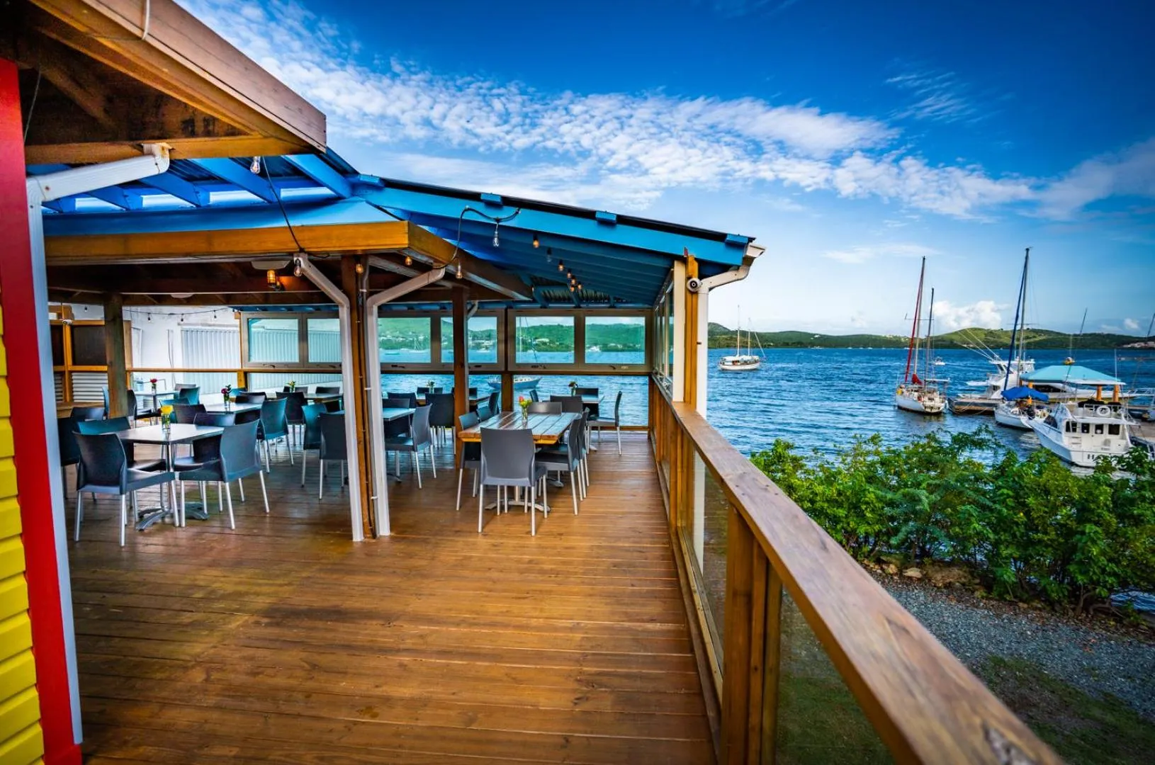 Terrasse en bois avec tables et chaises donnant sur une baie abritée.