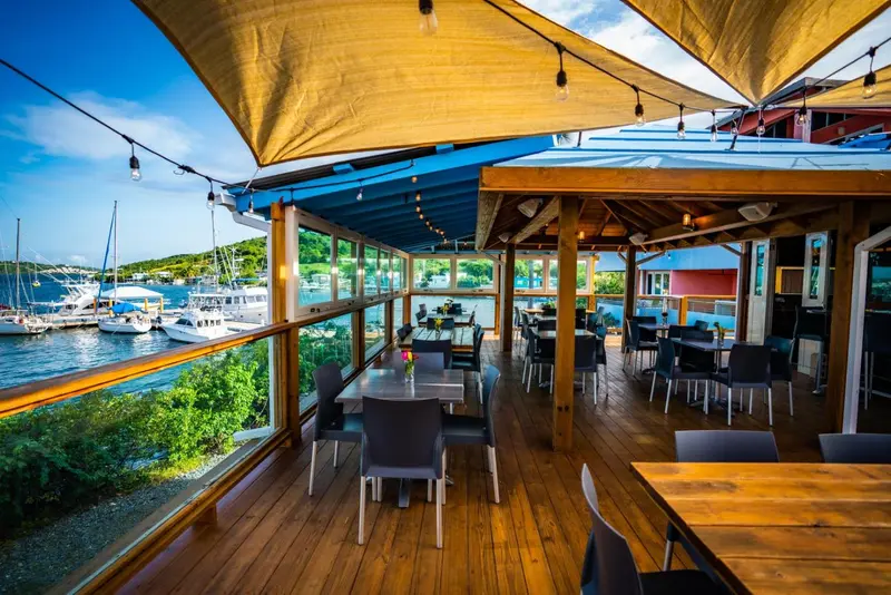 Une salle à manger lumineuse s'ouvre sur une terrasse en bois avec vue sur un port de plaisance.
