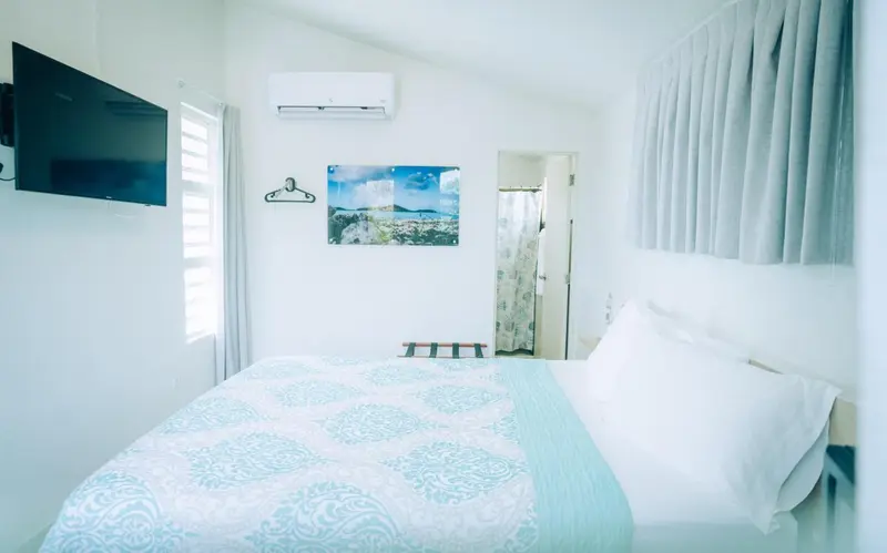 Une chambre lumineuse avec un lit recouvert d'une courtepointe turquoise et un téléviseur mural.