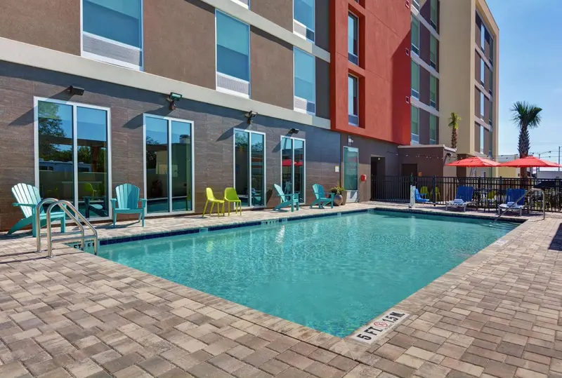 Piscine rectangulaire entourée d'une terrasse pavée avec des transats et des parasols.
