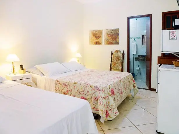 Une chambre lumineuse avec un lit recouvert d'une courtepointe fleurie et un accès à une salle de bain.