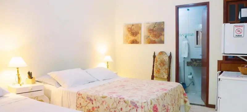 Une chambre lumineuse avec un lit recouvert d'une courtepointe florale et un accès à une salle de bain.