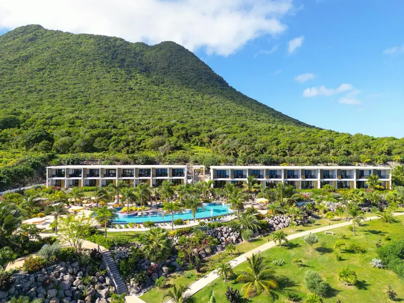 Vue aérienne d'un complexe hôtelier blanc bordant une piscine et une plage verdoyante.