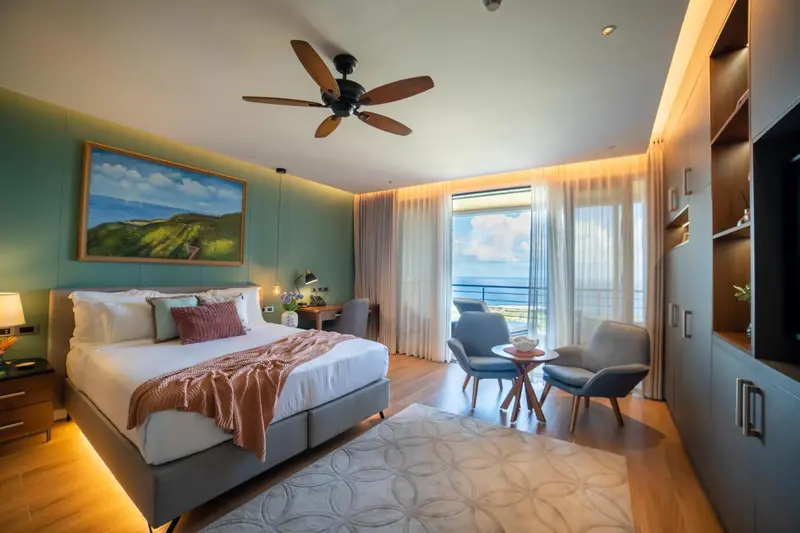 Une chambre lumineuse avec un grand lit et un coin salon donnant sur une vue mer.