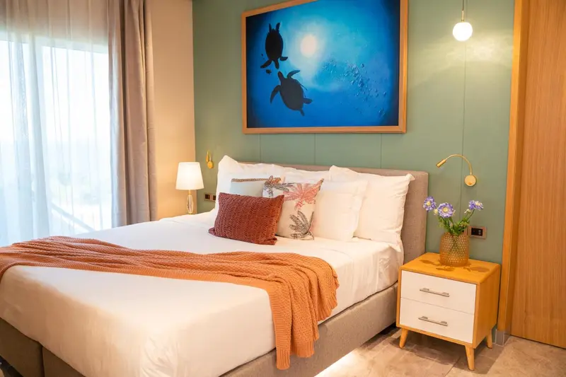 Une chambre lumineuse avec un grand lit recouvert d'une couverture orange et de coussins.