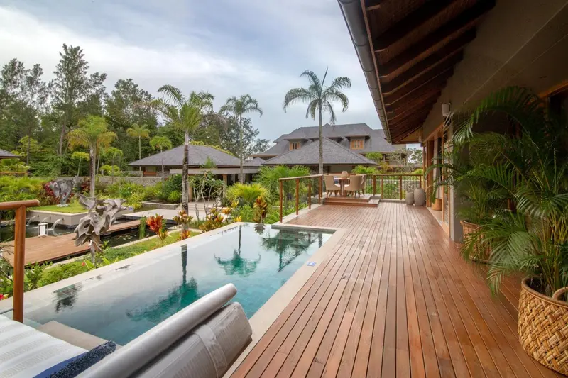 Terrasse en bois avec piscine et végétation luxuriante en arrière-plan.