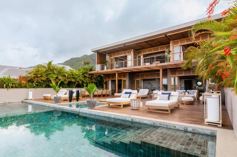 Terrasse en bois avec transats et piscine turquoise devant un bâtiment moderne.