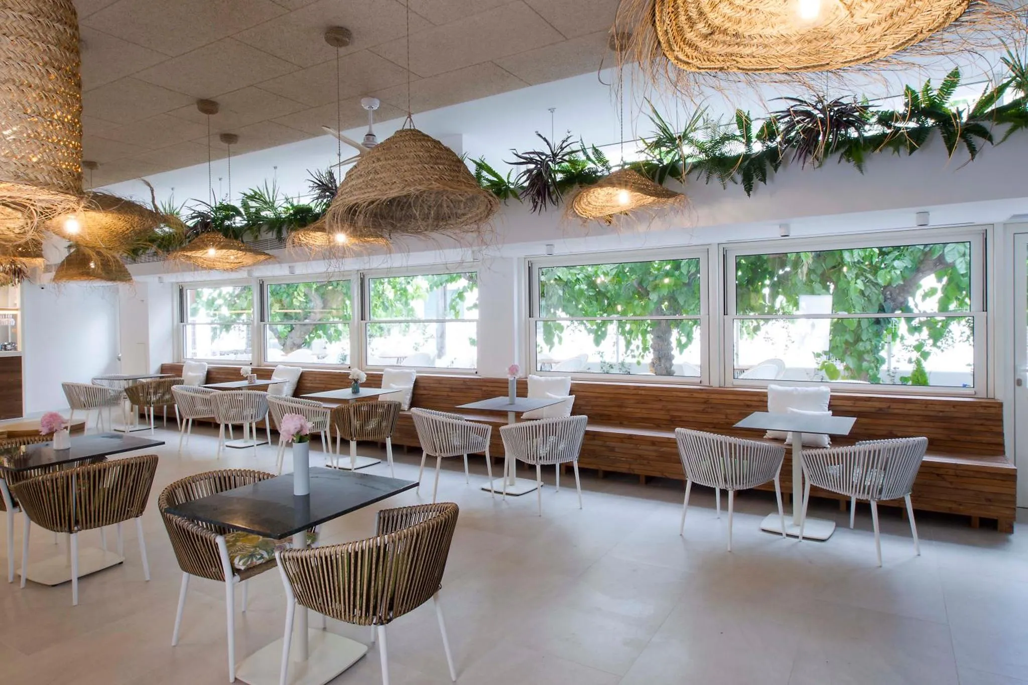 Une salle lumineuse avec des tables et des chaises en osier près de grandes fenêtres.