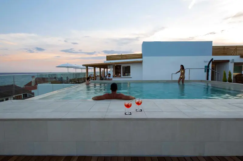 Une piscine à débordement surplombe la mer au coucher du soleil.