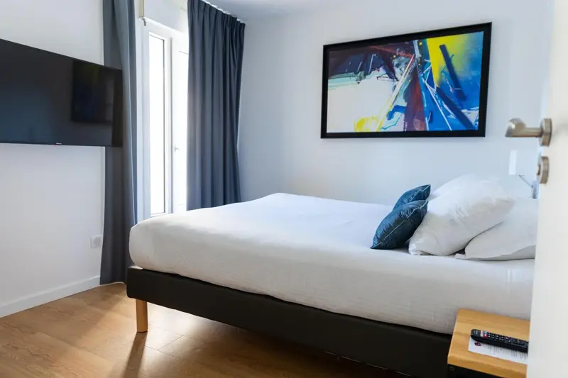 Une chambre lumineuse avec un grand lit et une télévision murale.